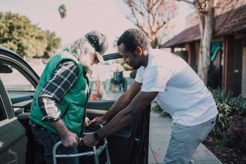 A Pensioner Being Helped From His Car