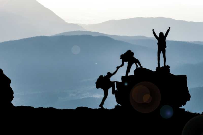 Three Climbers Reaching A Mountain Peak