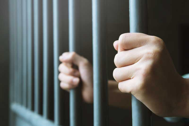 A Man In Prison Holding The Bars Of His Cell