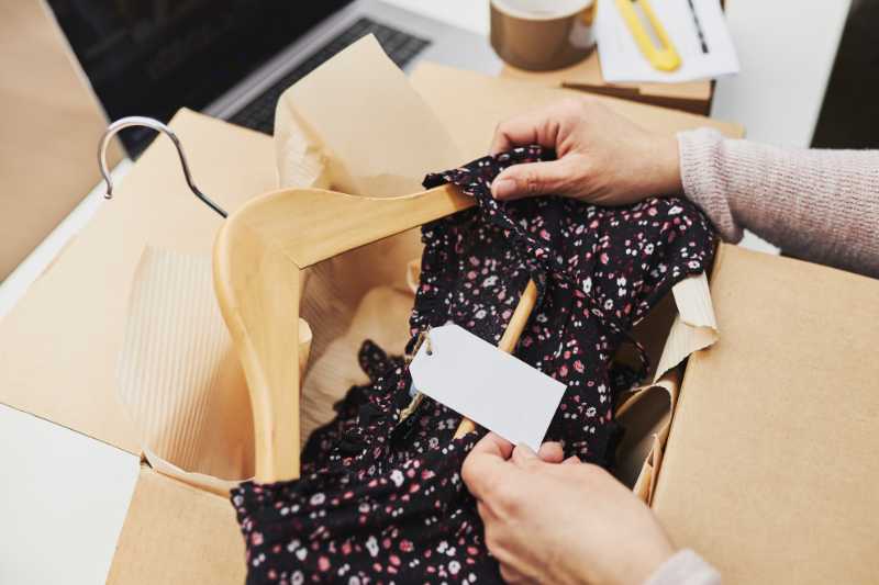 A Woman Holding The Label Of A Dress Which She Is Taking From A Cardboard Box