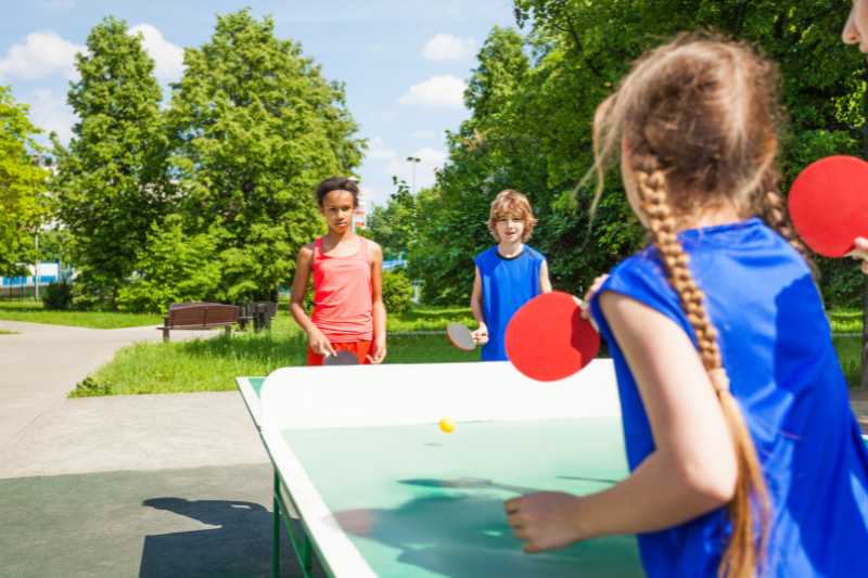 A Three Young Children Playing Table Tennis Outside