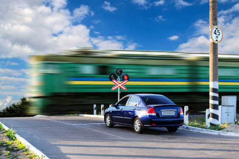 A Car Waiting At A Rail Crossing As A Train Passes