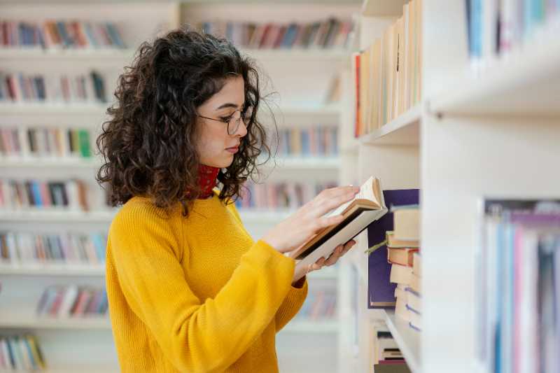 A Woman Looking At A Book In A Library