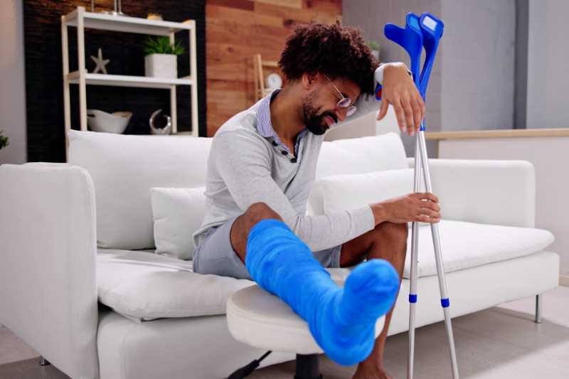 A Man With A Broken Leg Using Crutches To Help Lift Himself From The Sofa